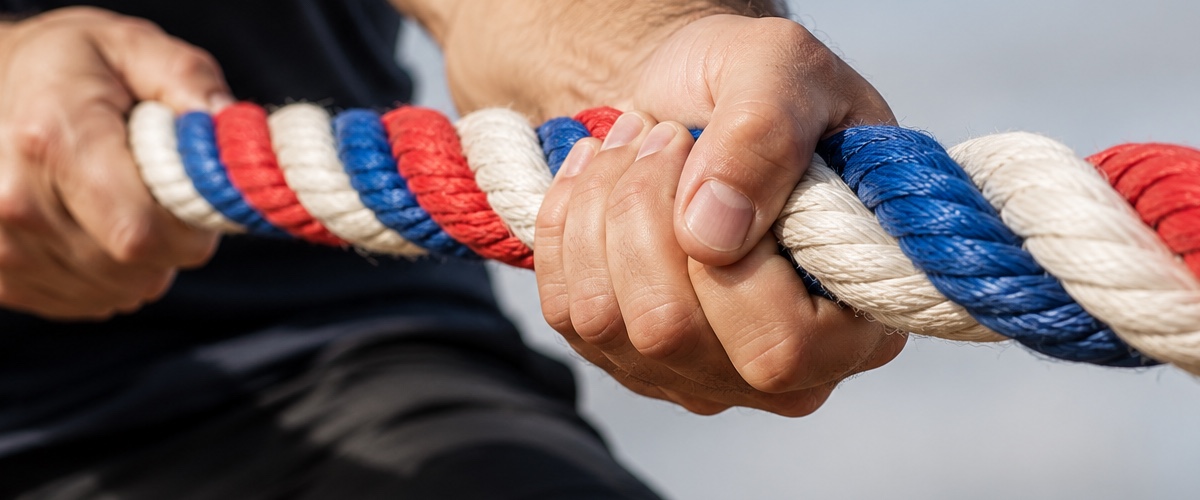 Hands gripping a thick braided rope of red, white and blue strands